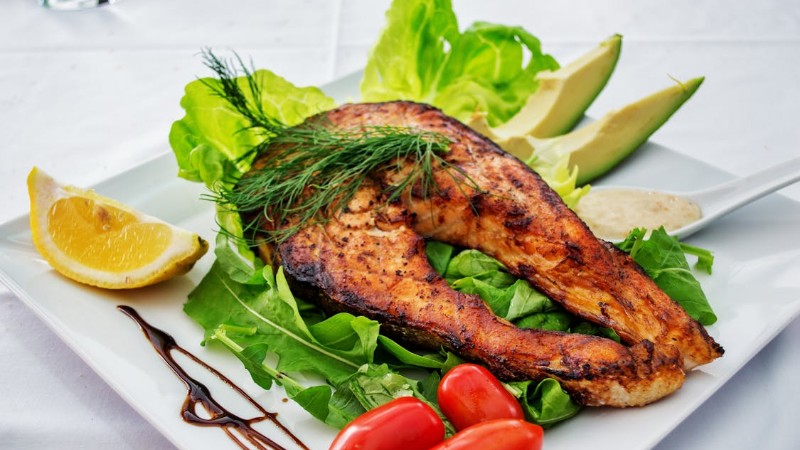 Delicious grilled salmon steak served with avocado, lettuce, cherry tomatoes, and lemon slice on a white plate., tags: verse wilde zalm voor - pexel